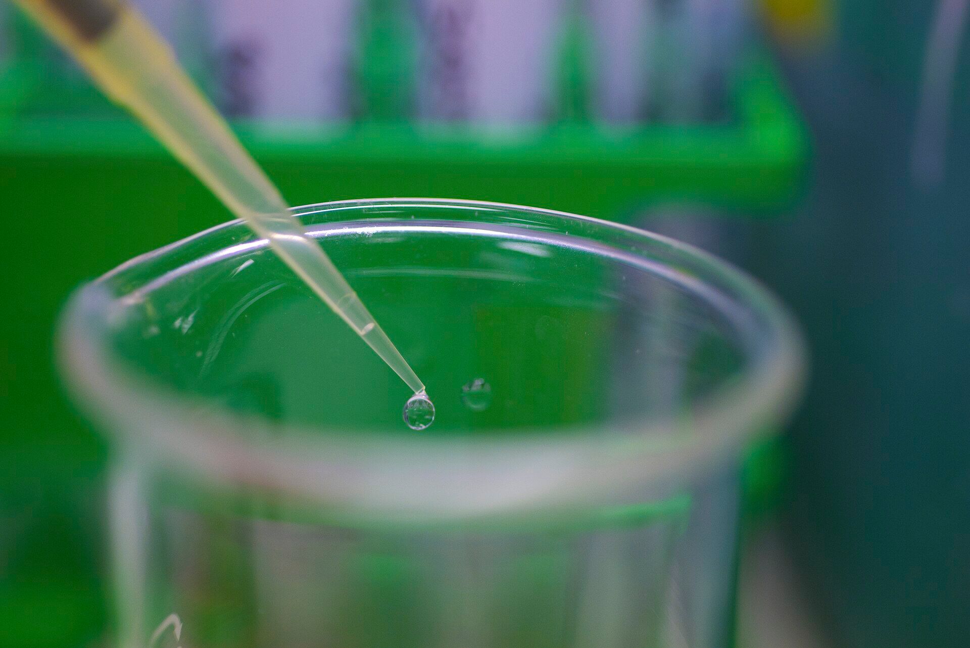 Gota de amostra na ponta de uma pipeta sobre um béquer, em laboratório com fundo verde